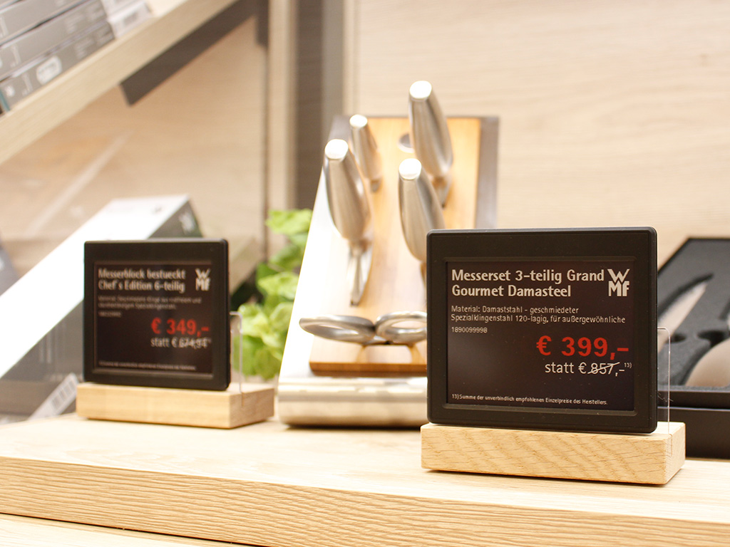 Elektronische Preisschilder auf Holzsockeln neben einem Messer-Display im Einzelhandel.